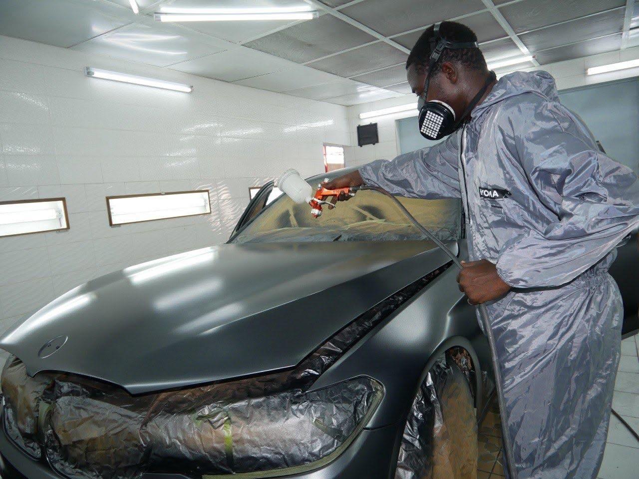 Technicien PMG CAR peignant un véhicule en cabine de peinture professionnelle à Abidjan