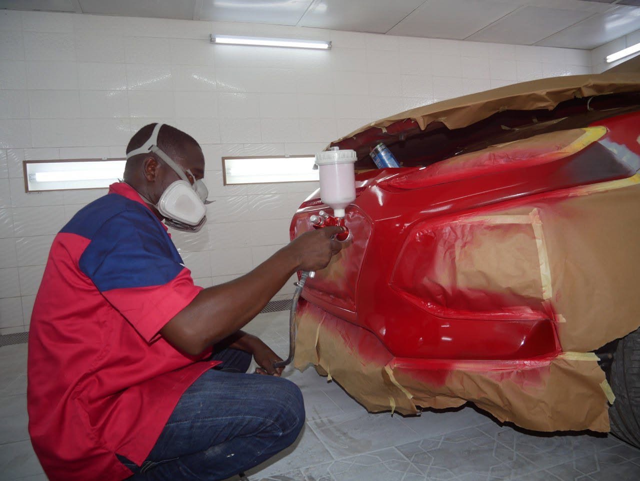 Technicien PMG CAR appliquant la peinture en cabine professionnelle